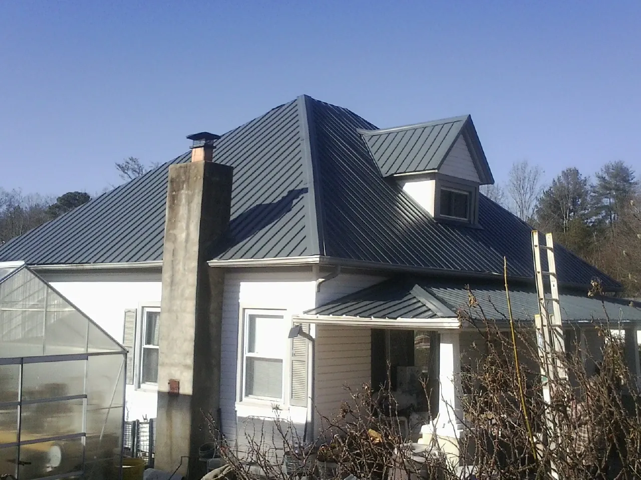 Dark blue standing seam metal roof on a white farmhouse with dormer — Slate & Tile Roof Repair by Roofing Brothers in Felton