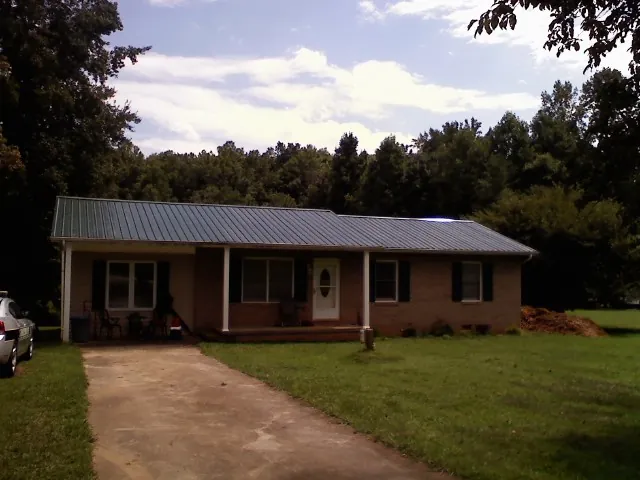 Dark green metal roof on a brick ranch with a covered porch in Felton