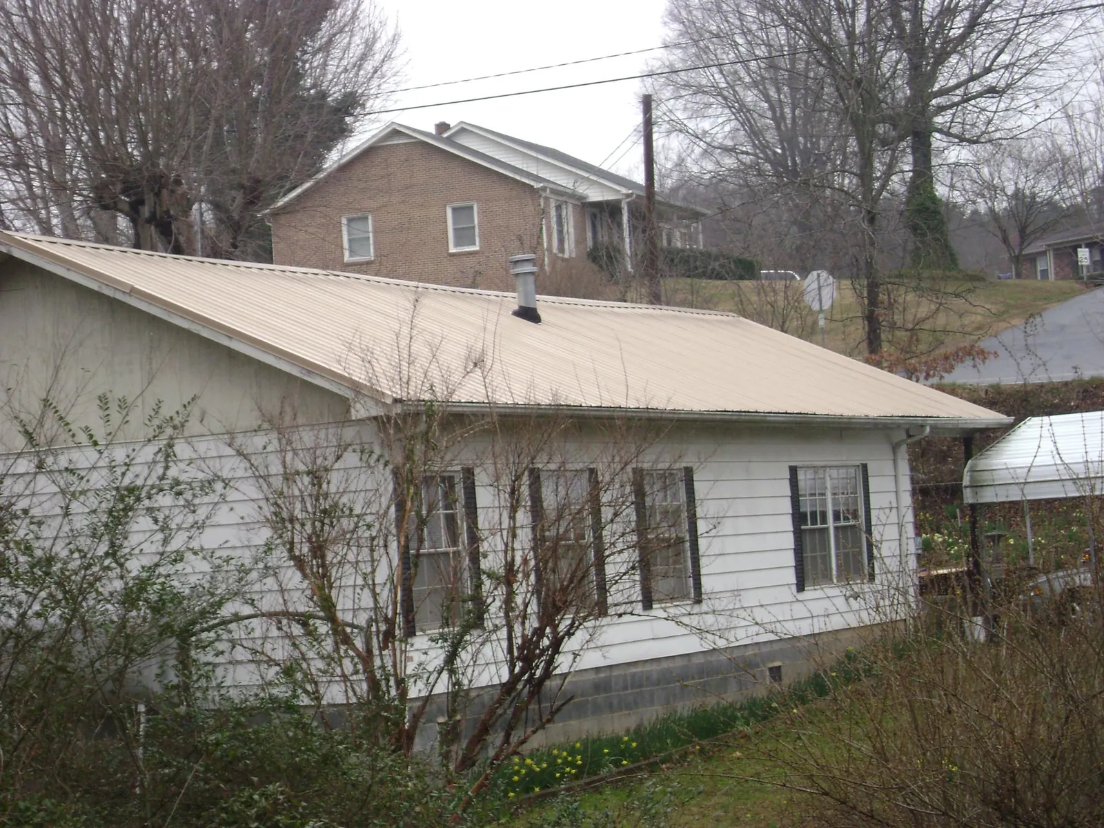Tan metal roof on a white sided house set into a hillside — Commercial Roofing by Roofing Brothers in Felton